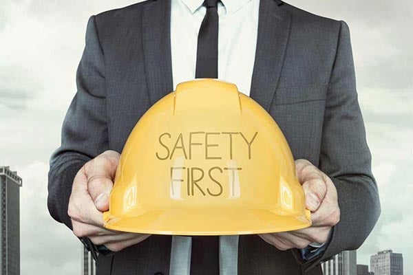 A person dressed in business attire holds out a hard hat that has the words &#x201C;safety first&#x201D; written on it.
