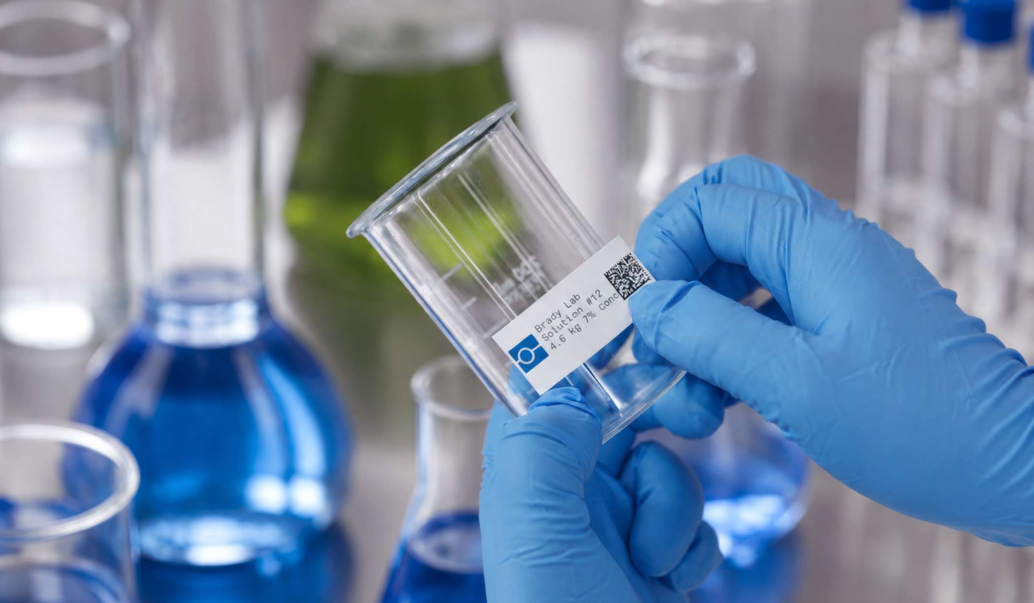 A lab technician applies a 2D barcode to a glass beaker