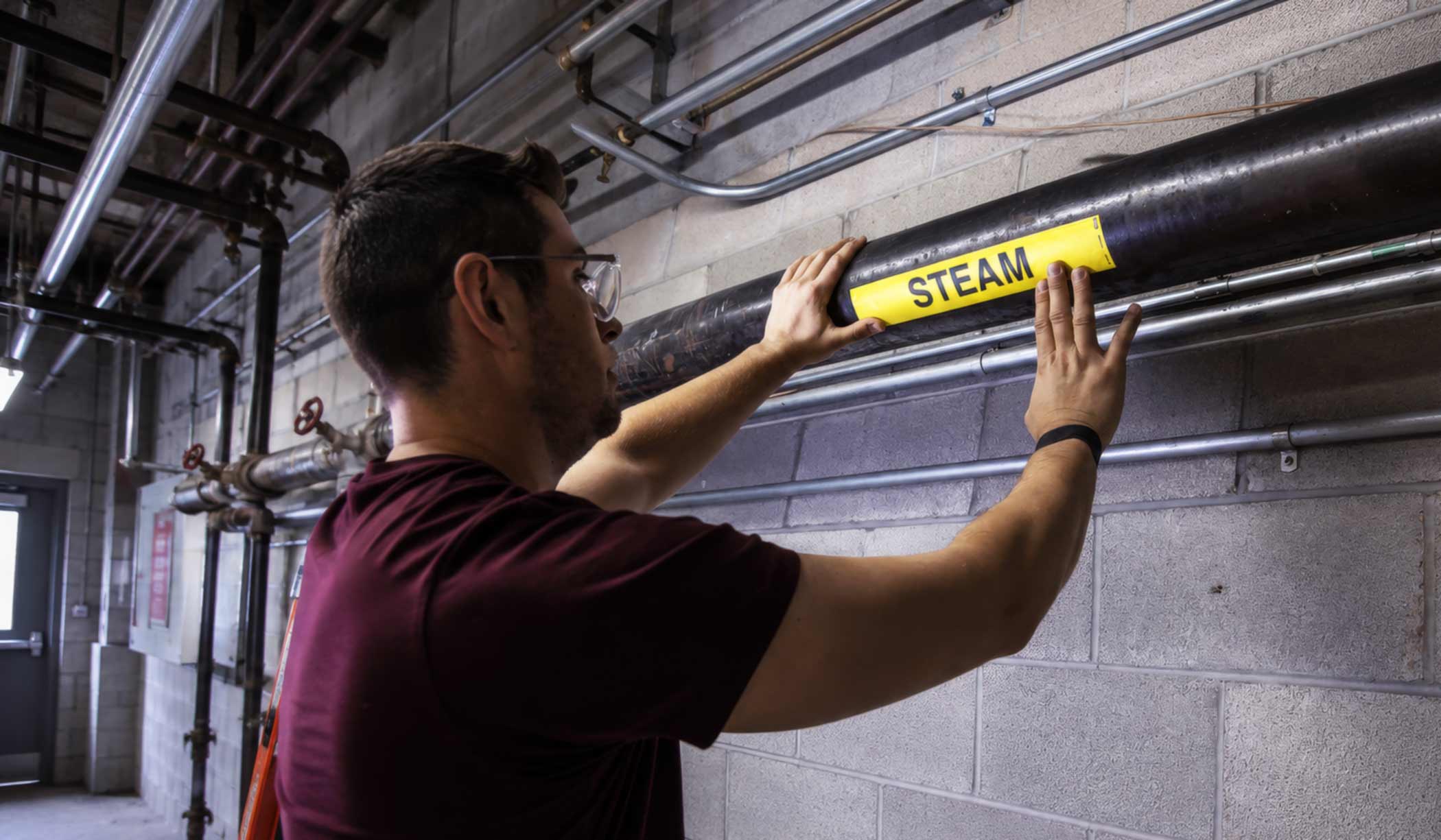 A maintenance worker applies a pipe marker to a steam vent