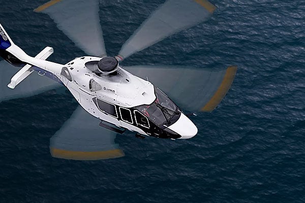 A white Airbus helicopter hovers over water.
