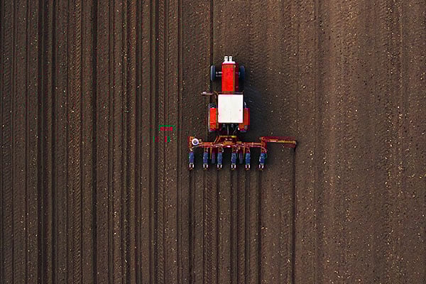 Extreme overhead perspective of red tractor tiling a field.