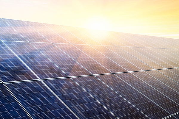 Closeup of solar panels with sun in the background.