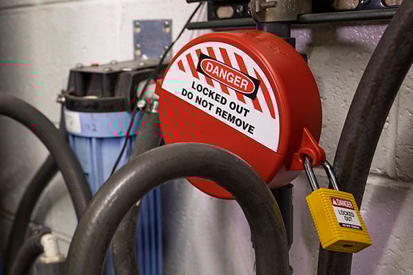 Red lockout device with yellow padlock on industrial pipes.
