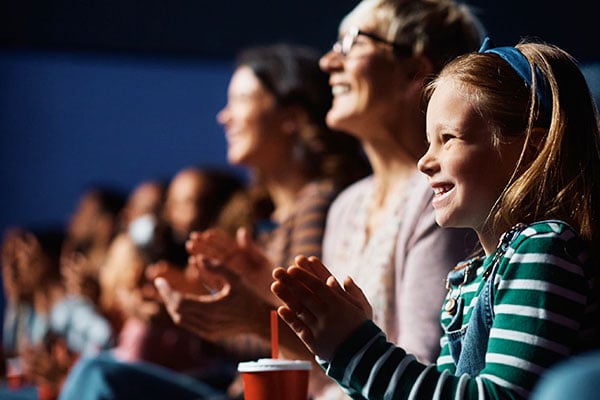 Side view of audience row in theater clapping and smiling.
