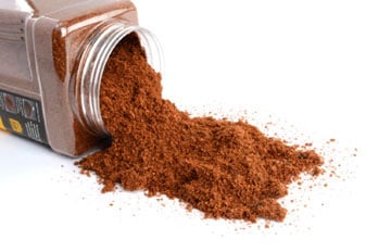 Small container of reddish-brown spice spilling onto a surface. 