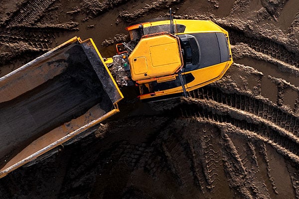 Overhead view of yellow dump truck driving on packed dirt. 