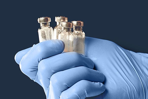 Closeup of a blue gloved hand holding clear sample vials.