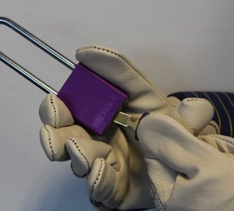 Closeup of gloved hands inserting key in purple padlock.