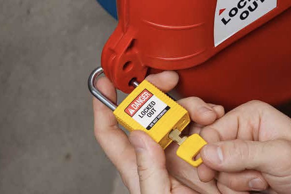 Hands unlocking a yellow lockout padlock from a red industrial lockout device.