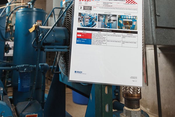  A printed Lockout/Tagout procedure sheet with photos hanging in front of industrial machinery.