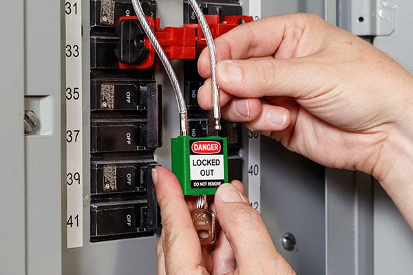  Hands apply a cable lockout device and a padlock to a circuit breaker panel.