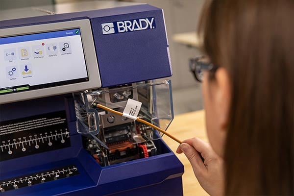 A wire with a label applied to it in front of a Wraptor A6500 printer.