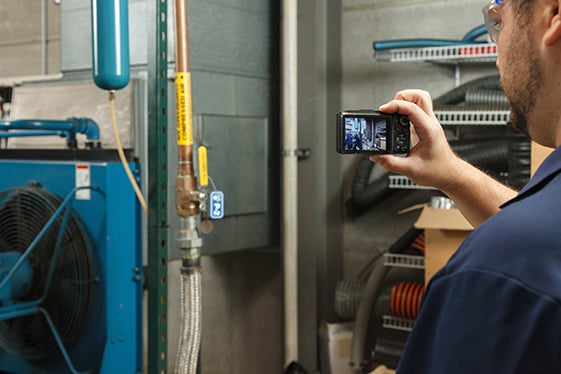 A man taking a photograph of a lockout point within a manufacturing plant.