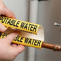 A wrap around potable water pipe marker being applied to a water pipe.