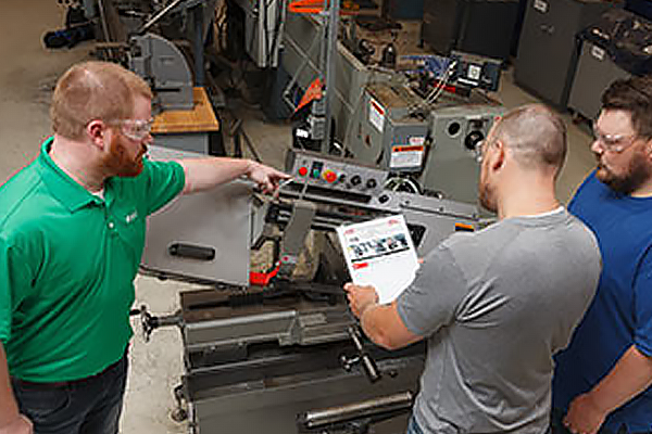 Instructor showing a machine control panel to two workers reviewing a LOTO procedure.