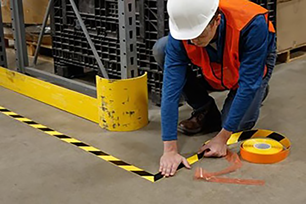 A worker marking an area in a manufacturing facility with yellow and black striped tape.