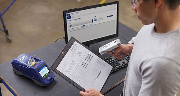 Man scanning barcodes on a piece of paper with a Brady label printer and computer in background