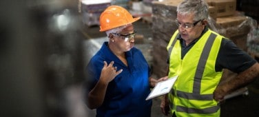 Two workers discuss processes in a factory or warehouse. 