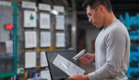 A man scans a document with a handheld Brady scanner in an industrial setting. 