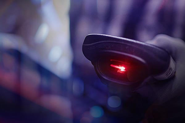 Artistic photo of hand holding a barcode scanner with red laser light.