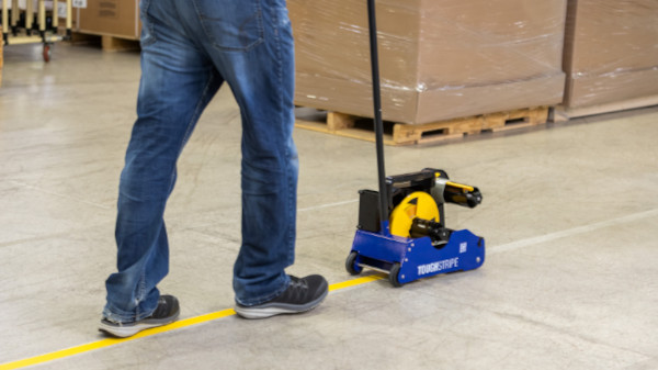 Employee laying yellow floor tape with a Brady Floor Tape Applicator.