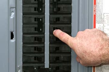 Hand pointing to a specific circuit breaker in a breaker panel.