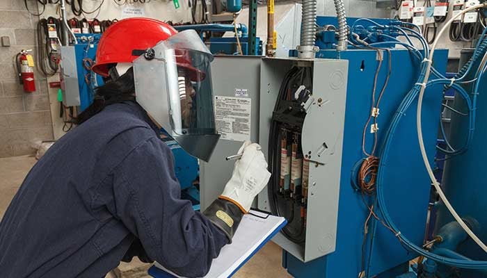 Worker in safety gear inspects an electrical panel.