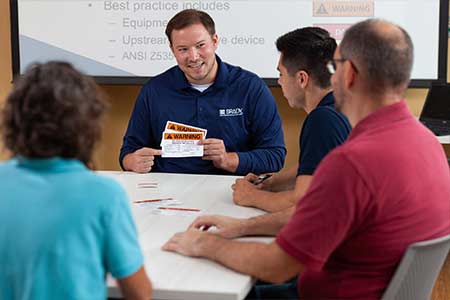 Manager instructs a group of employees while holding safety signs.