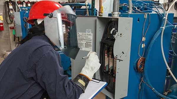A woman with a face shield inspects an electrical panel.