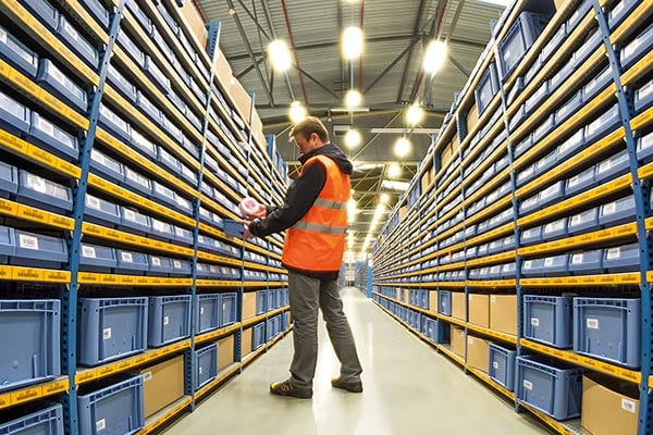 Warehouse aisle with storage shelving and worker organizing items.
