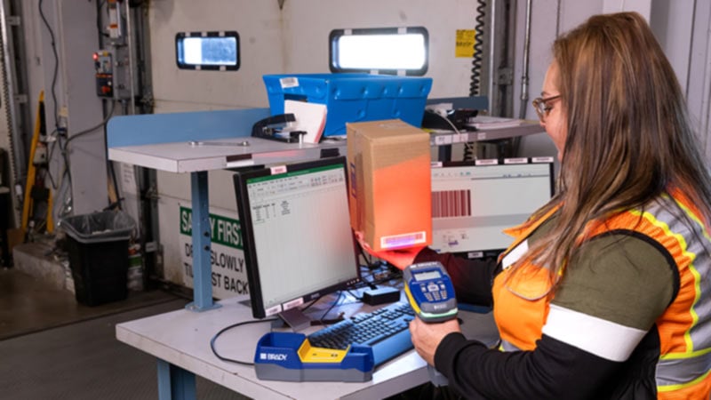 Female worker in safety vest sits at table scanning barcodes.