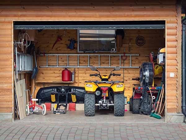 Front of an open garage holding an ATV and plow plus tools.