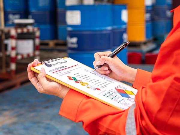 Worker in PPE reviews hazardous chemical notes on a clipboard.