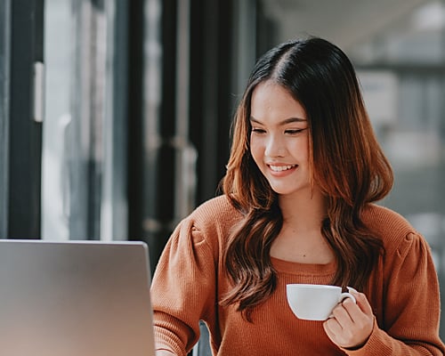 Closeup of woman working on a laptop with teacup.