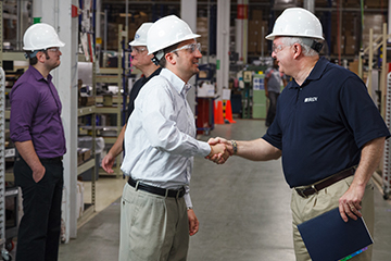 A Brady employee on a factory floor shaking hands.