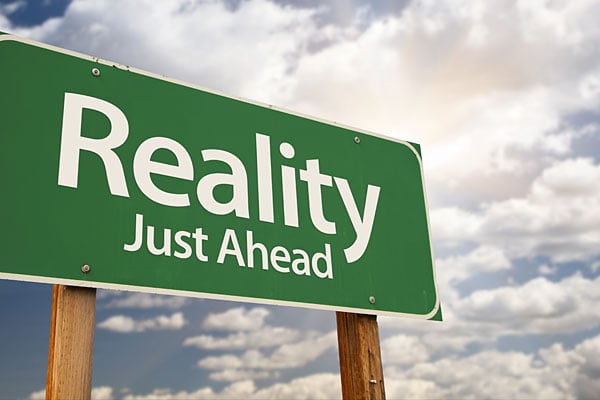 Green road sign reading &quot;Reality Just Ahead.&quot; 