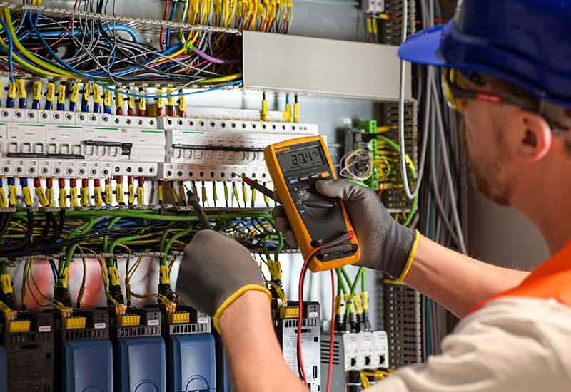 Man in gloves testing wiring with meter.