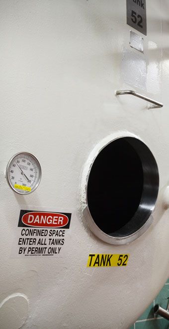 A white tank with a black opening, pressure gauge, and warning label.
