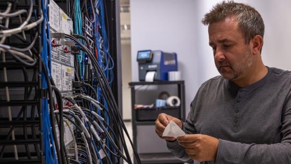 A data center technician uses a Brady i7500 label printer to apply cable labels to network cables.