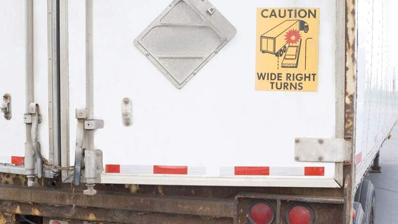 A sign reading caution wide right turns on back of semi truck.