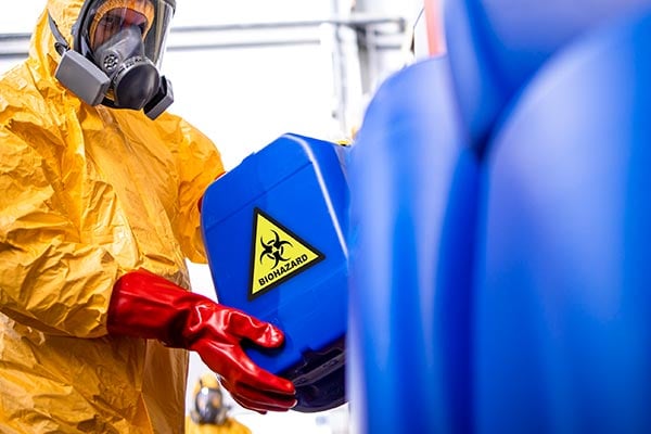 Worker in haz mat suit, mask and gloves with biohazard container. 