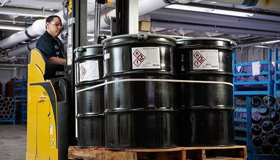 Worker inspecting chemical drums on a pallet.