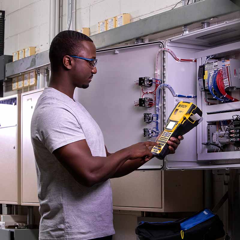 Worker at an electrical panel operating a Brady M410 industrial label printer. 