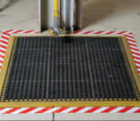 A square floor drain surrounded by red and white striped floor tape.