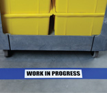 Yellow bins on a cart with blue floor tape marking the area as work in progress.