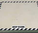 An area marked with black and white striped floor tape and a label reading keep clear.