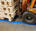 A fork lift and pallets behind an area marked with blue floor tape.