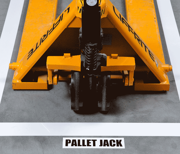 A piece of equipment surrounded by white floor tape and a label reading pallet jack.