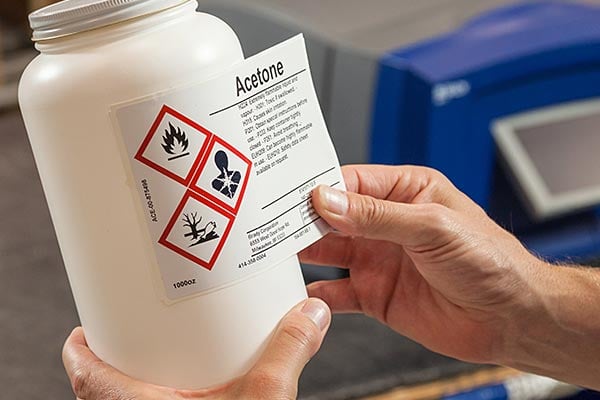 Worker placing a GHS warning label on a bottle.