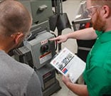 Two workers perform safety services on a machine.